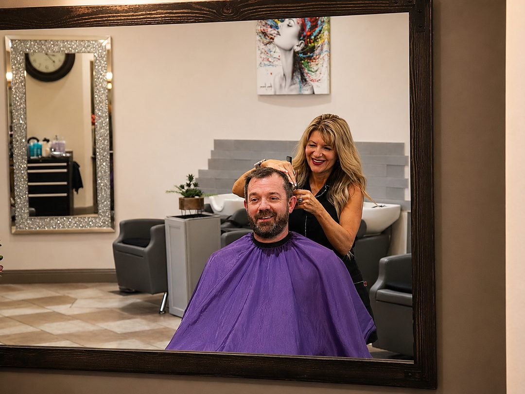 Cindy cutting a client's hair, seen in the salon mirror