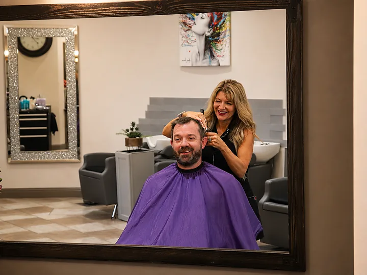 Cindy cutting a client's hair, seen in the salon mirror